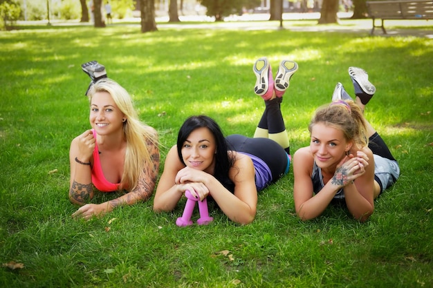 3人の陽気な女性の友人が屋外の公園の芝生に横たわり、トレーニング後にリラックスします