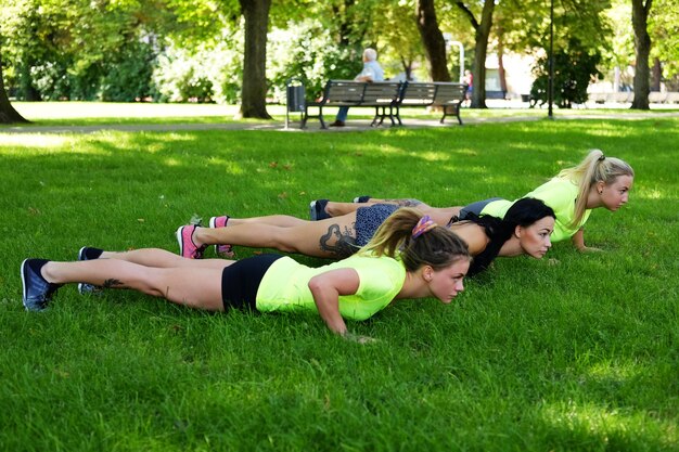 Три спортивные женщины разогреваются на лужайке в летнем парке.