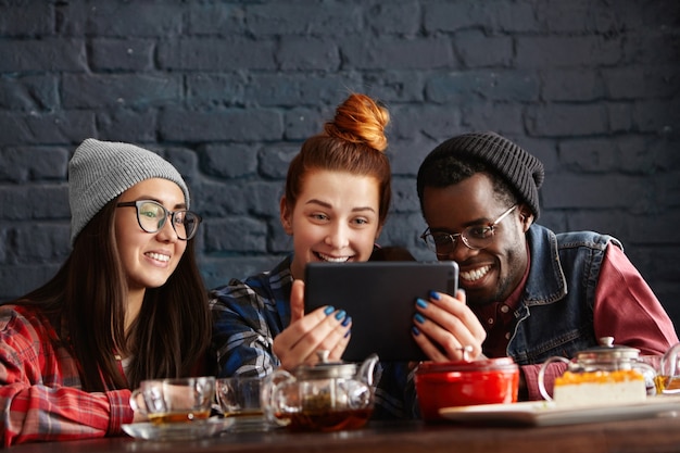 Three students enjoying free wi-fi, using digital tablet at cafe during lunch break