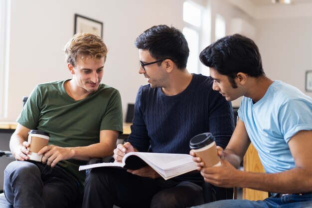 Three students reading textbook together, talking and drinking