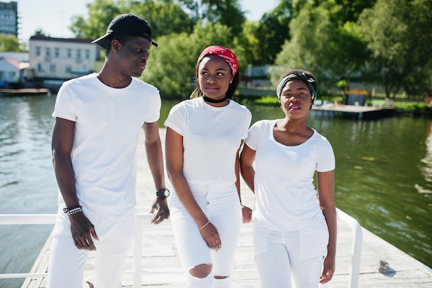 Three stylish african american friends wear on white clothes at pier on beach Street fashion of young black people Black man with two african girls