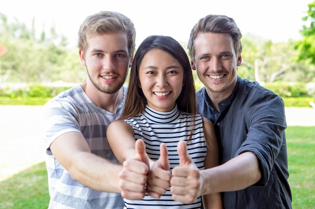 Три успешных студента друзья показывая пальцы вверх