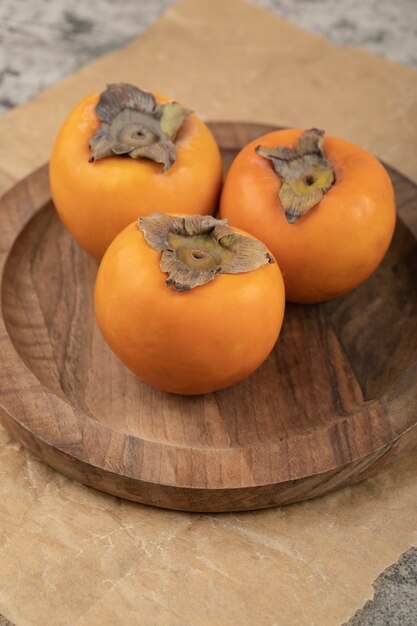 大理石の表面の木板に3つのおいしい冬柿