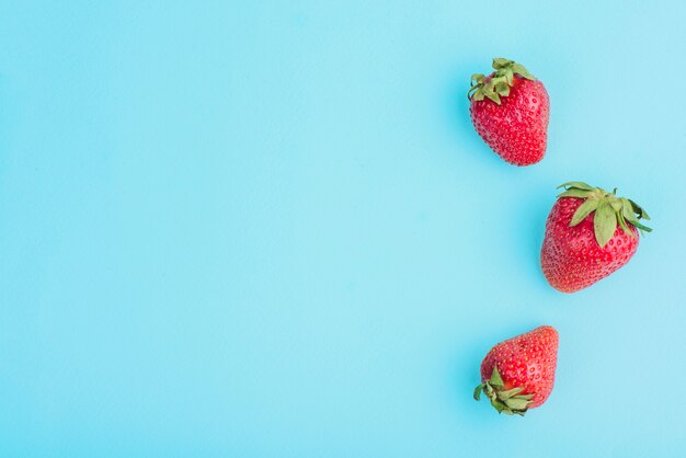 Three tasty strawberries on blue surface
