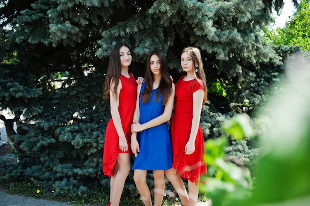 青と赤のドレスを着た3人のティーンエイジャーの女の子が屋外でポーズをとった