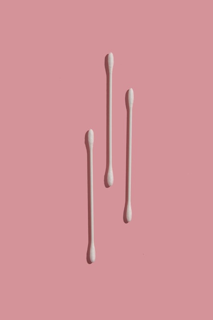 Three thin cotton swabs on pink background top view from above