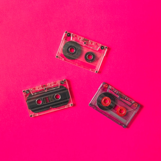 ピンクの背景に3つの透明なカセットテープ