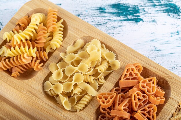 Free photo three types of dry pasta placed on wooden plate.