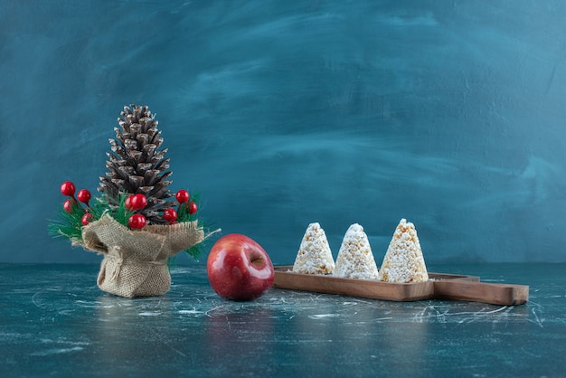 Three vanilla-coated cakes, an apple and a christmas ornament on blue.