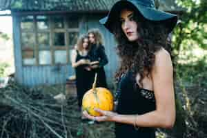 Free photo three vintage women as witches, pose in front of an abandoned building on the eve of halloween