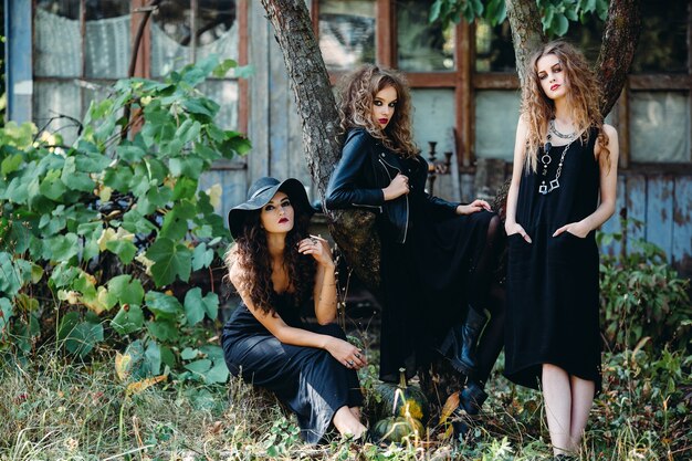 Three vintage women as witches, pose in front of an abandoned building on the eve of Halloween