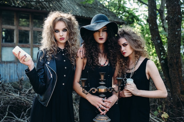 Three vintage women as witches, pose in front of an abandoned building on the eve of Halloween