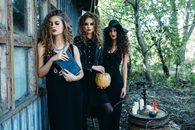 Three vintage women as witches, poses near an abandoned building on the eve of Halloween