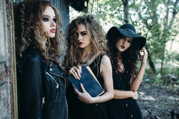 Free photo three vintage women as witches, poses near an abandoned building on the eve of halloween