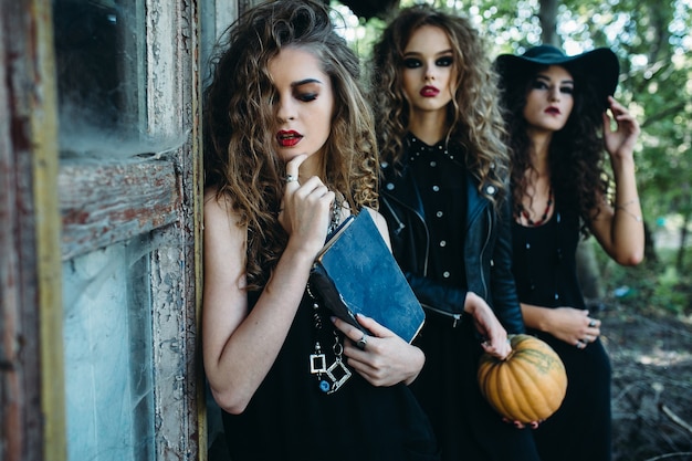 Tre donne vintage come streghe, posano vicino a un edificio abbandonato alla vigilia di halloween