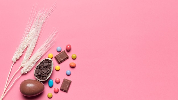 Tre spighe di grano con cioccolato uova di pasqua e gemme caramelle su sfondo rosa