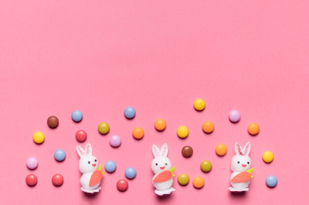Three white bunnies with colorful gem candies on pink background