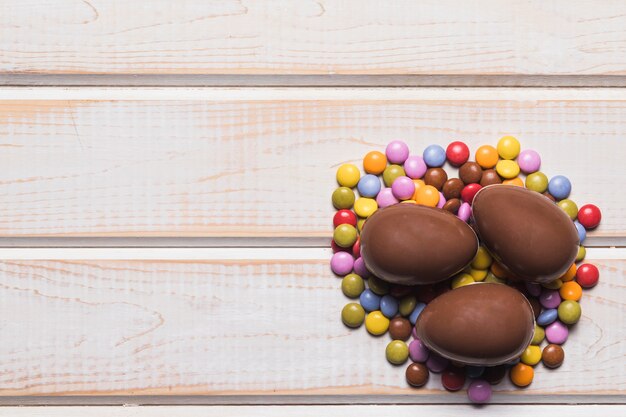 Free photo three whole chocolate easter eggs on gems candies on wooden table