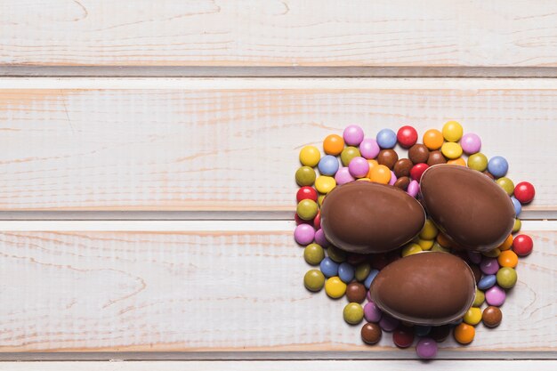 Three whole chocolate easter eggs on gems candies on wooden table