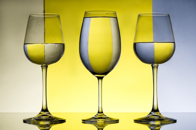 Three wineglasses with water over grey and yellow wall