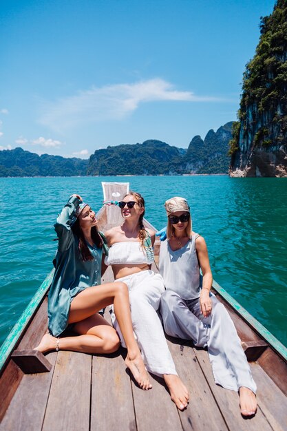 Three woman tourists friends travel around Khao Sok national park, on vacation in Thailand. Sailing on asian boat on lake at sunny day, with amazing view.