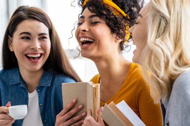 Three women laughing together with book and cup of coffee