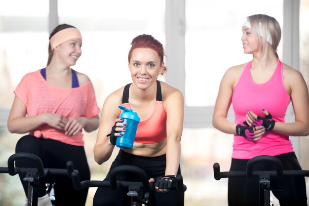 Three women relaxing after cardio exercises on cycles