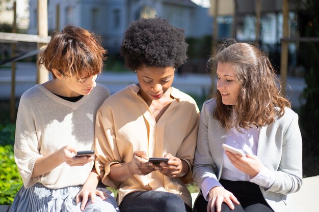 Three women with smartphones sitting on street