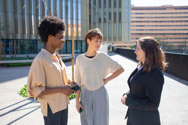 Three women with smartphones standing on street