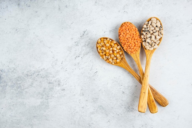 Free photo three wooden spoons of raw beans on a marble table.