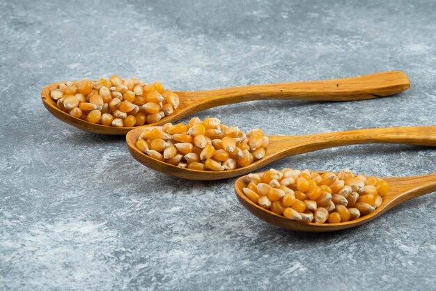 Three wooden spoons of raw corns on marble surface.