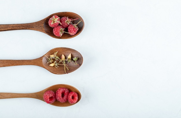 three wooden spoons of red raspberries and dry leaves on stone surface