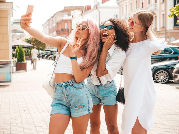 Three young beautiful smiling female in trendy summer clothesSexy carefree multiracial women posing on the street backgroundPositive models having fun in sunglasses Cheerful and happy