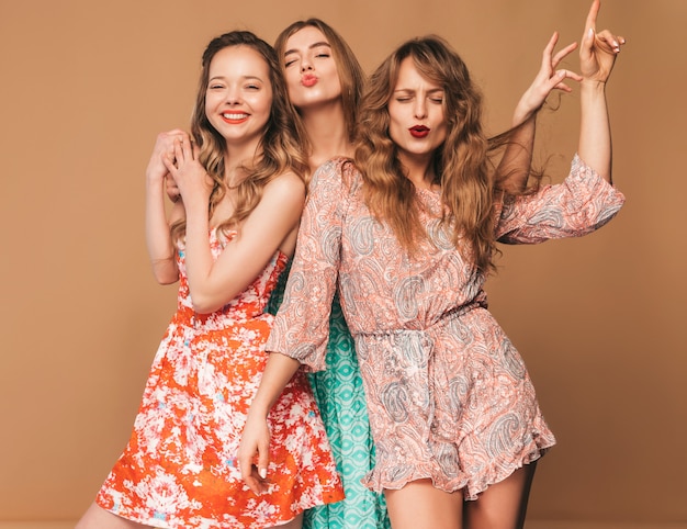 Три молодые красивые улыбающиеся девушки в модных летних повседневных платьях и в солнцезащитных очках. Сексуальные беззаботные женщины позируют.