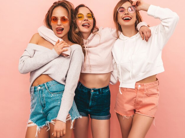 Three young beautiful smiling girls in trendy summer clothes. Sexy carefree women posing. Positive models having fun. Hugging and showing tongue