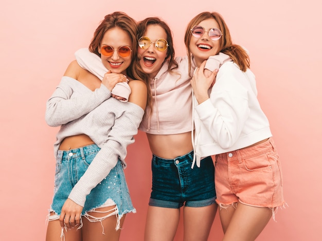 Three young beautiful smiling girls in trendy summer clothes. Sexy carefree women posing. Positive models having fun. Hugging