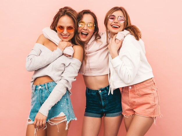Три молодые красивые улыбающиеся девушки в модной летней одежде. Сексуальные беззаботные женщины позируют. Позитивные модели с удовольствием. В обнимку