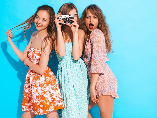 Three young beautiful smiling girls in trendy summer colorful dresses. Sexy carefree women posing. Taking pictures on retro camera