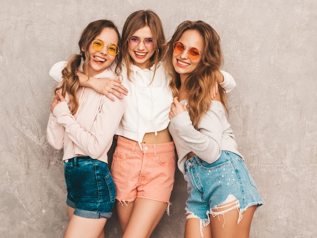 Three young beautiful smiling girls in trendy summer sport clothes. Sexy carefree women posing. Positive models in round sunglasses having fun. Hugging