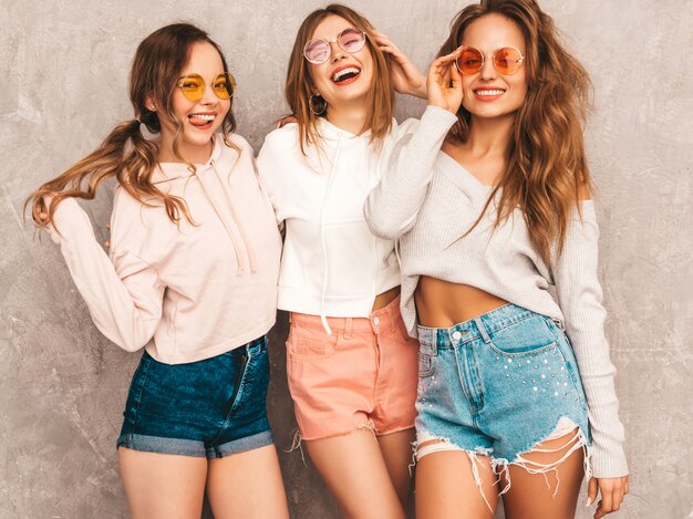 Three young beautiful smiling girls in trendy summer sport clothes. Sexy carefree women posing. Positive models in round sunglasses having fun. Hugging