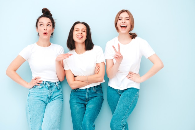 Три молодые красивые улыбающиеся хипстерские девушки в модной той же летней белой футболке и джинсовой одежде