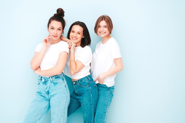 Три молодые красивые улыбающиеся хипстерские девушки в модной той же летней белой футболке и джинсовой одежде