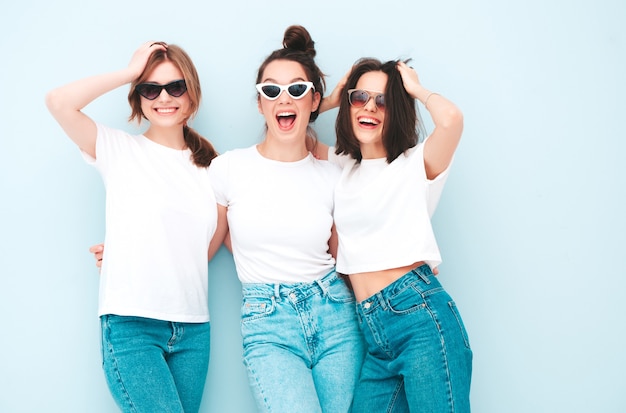 トレンディな同じ夏の白いTシャツとジーンズの服を着た3人の若い美しい笑顔の流行に敏感な女性