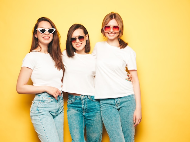 トレンディな同じ夏の白いTシャツとジーンズの服を着た3人の若い美しい笑顔の流行に敏感な女性