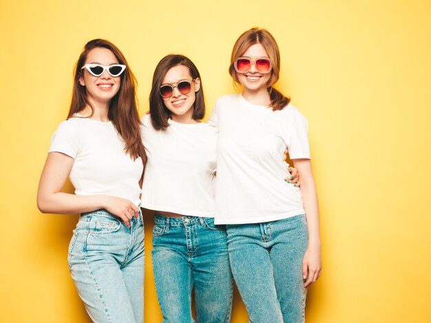 Three young beautiful smiling hipster female in trendy same summer white t-shirt and jeans clothes