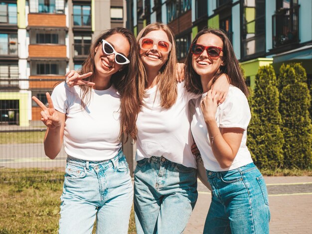 トレンディな夏の同じ服を着た3人の若い美しい笑顔のヒップスター女性通りの背景でポーズをとるセクシーな屈託のない女性サングラスで楽しんでいるポジティブモデル陽気で幸せな抱擁