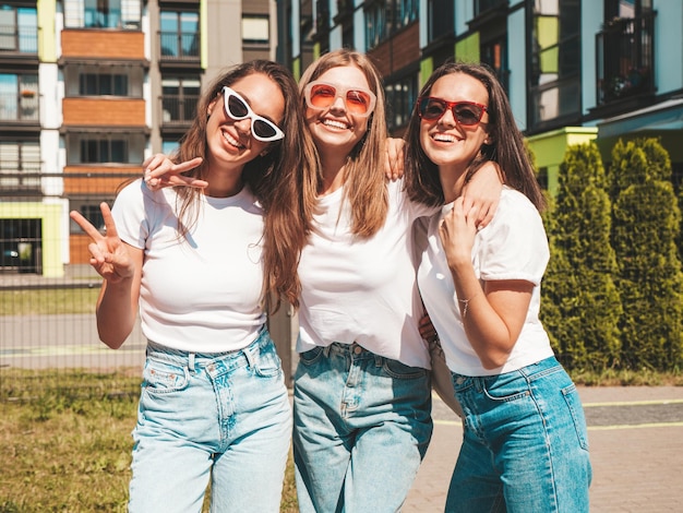 Three young beautiful smiling hipster female in trendy summer same clothes Sexy carefree women posing on the street backgroundPositive models having fun in sunglassesHugging Cheerful and happy