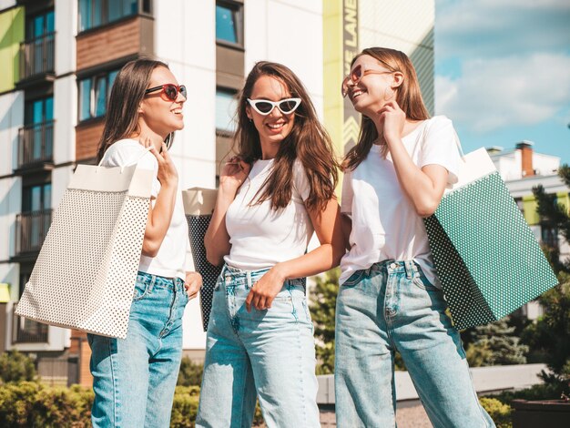 Три молодые красивые улыбающиеся женщины-хипстеры в модной летней одинаковой одежде Сексуальные беззаботные женщины позируют на фоне улицы.