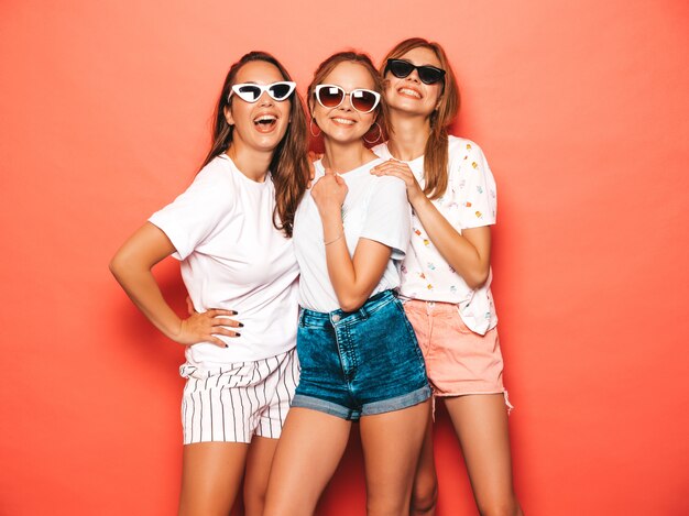 Три молодые красивые улыбающиеся битник девушки в модной летней одежде. Сексуальные беззаботные женщины позируют возле розовой стены. Позитивные модели сходят с ума и веселятся. В солнцезащитных очках