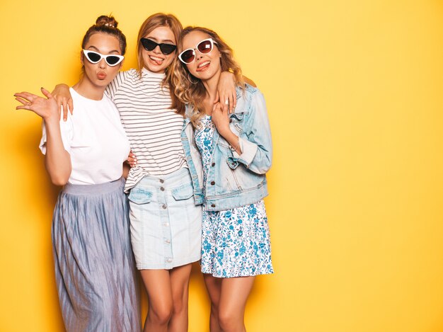 최신 유행의 여름 옷을 입고 세 젊은 아름 다운 웃는 hipster 여자. 노란 벽 근처 포즈 섹시 평온한 여자입니다. 선글라스 재미있는 긍정적 인 모델